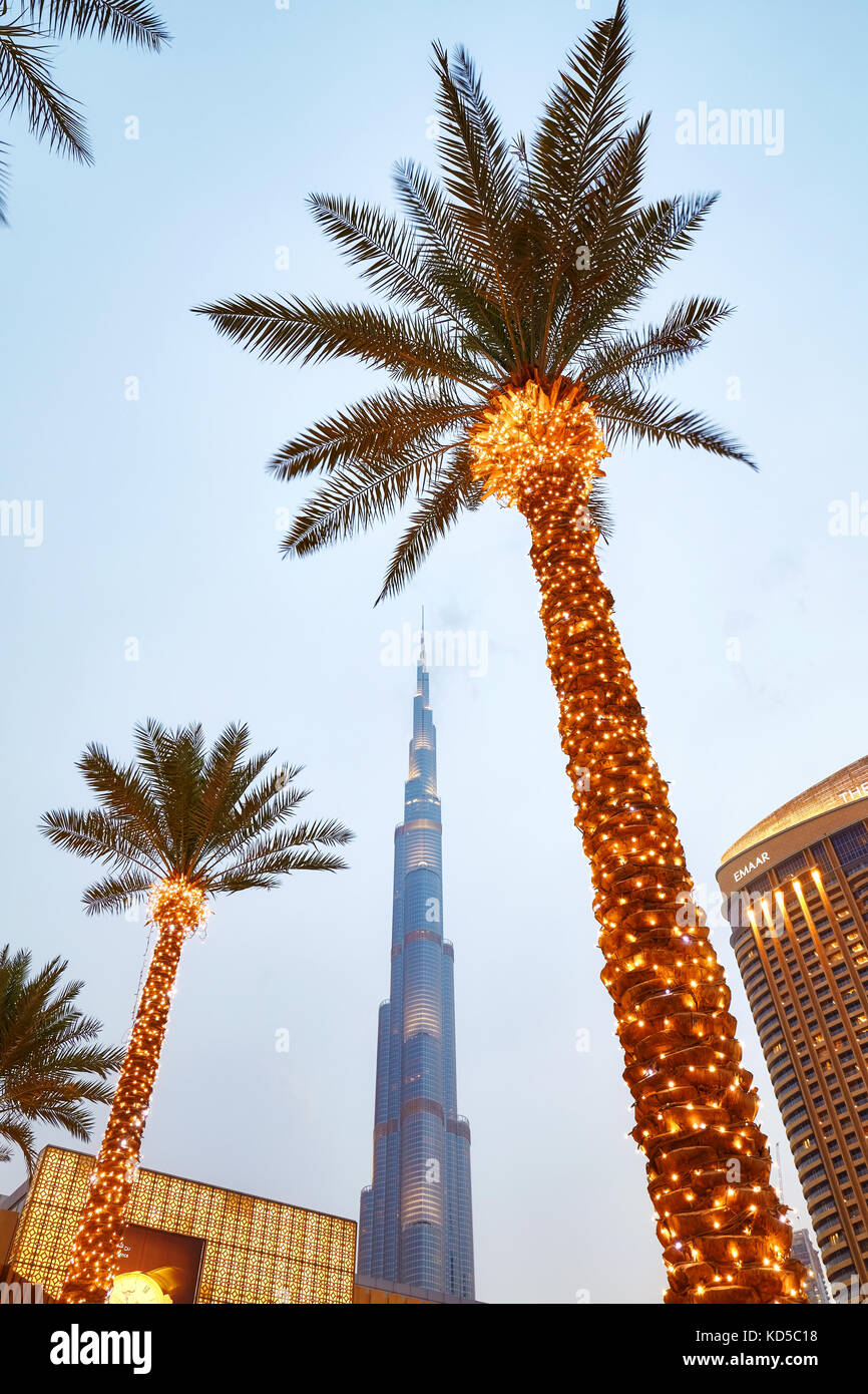 Dubai, United Arab Emirates - May 1, 2017: Looking up view of illuminated palm trees, Dubai Mall and Burj Khalifa facade at dusk. Stock Photo