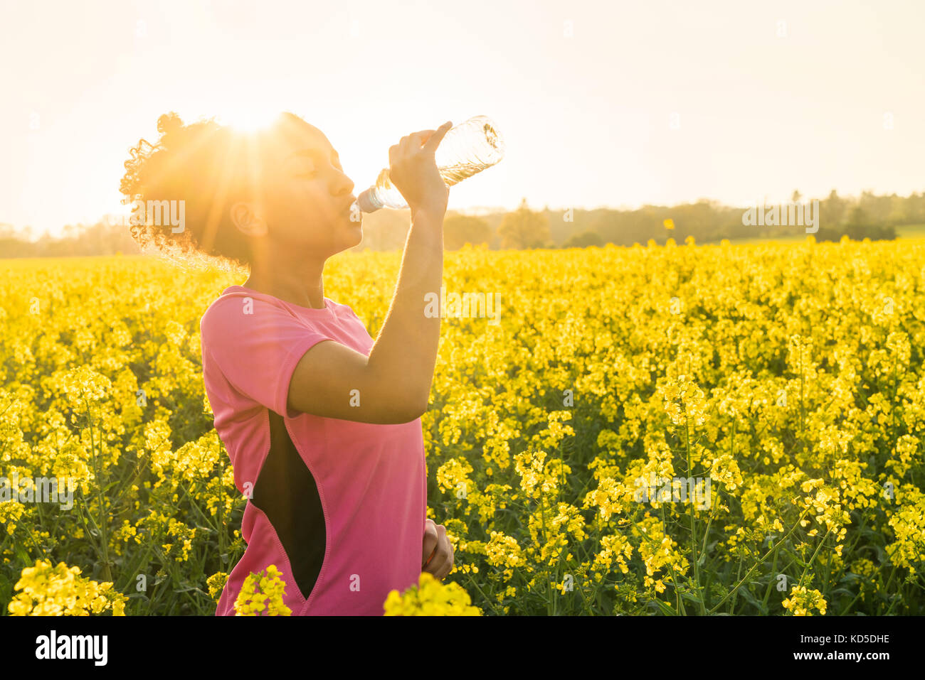 Outdoor portrait of beautiful happy mixed race African American girl teenager female young woman athlete runner drinking water from a bottle in a fiel Stock Photo