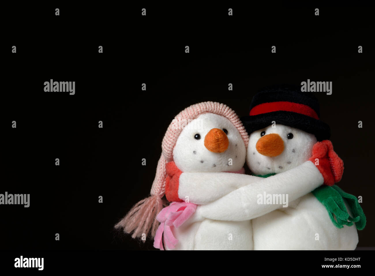 Two hugging snowmen on black background representing warmth and happiness isolated against monochromatic background.Studio shot. Stock Photo