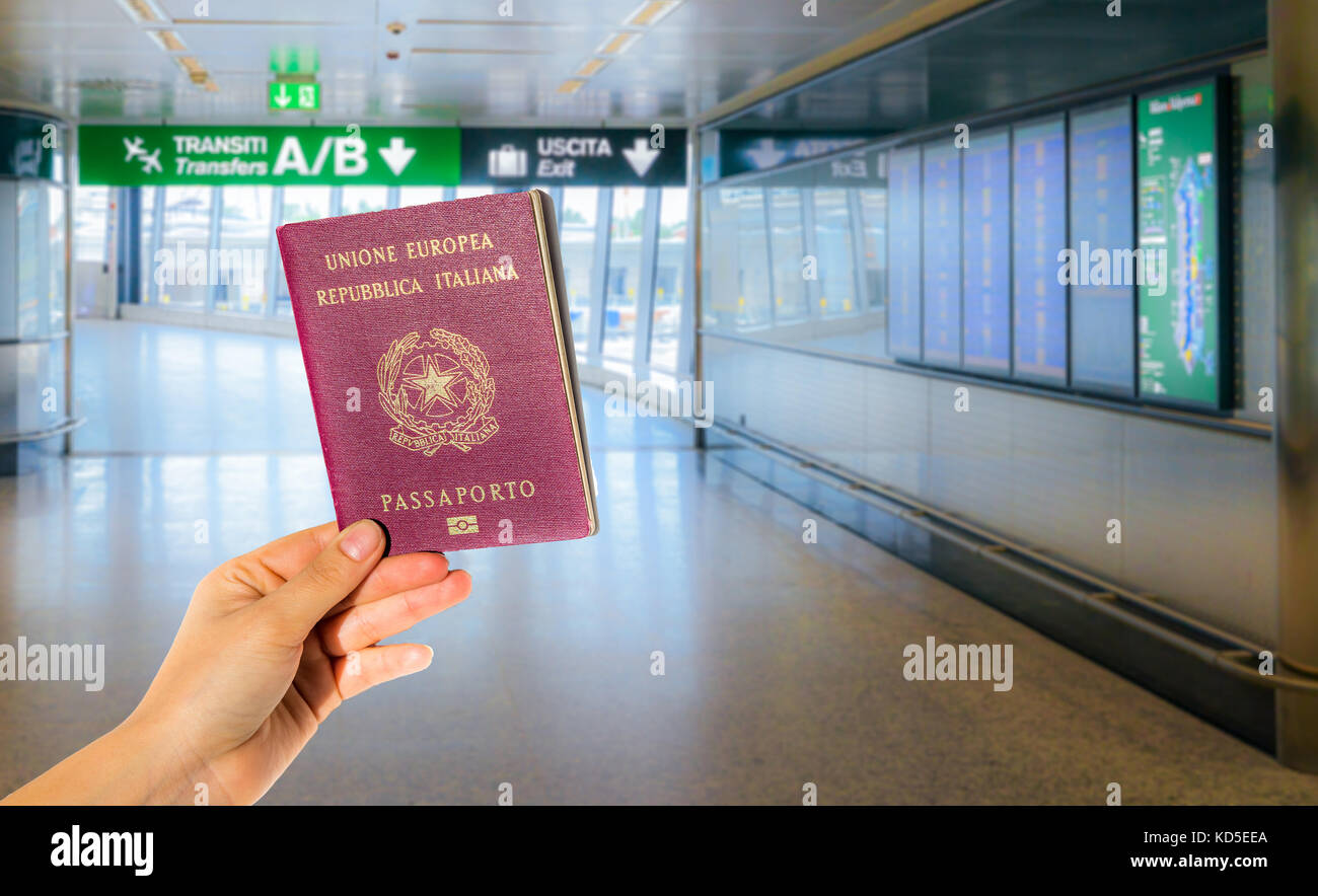 Person holding an Italian passport at an Italian airport with flight information panels on the right Stock Photo