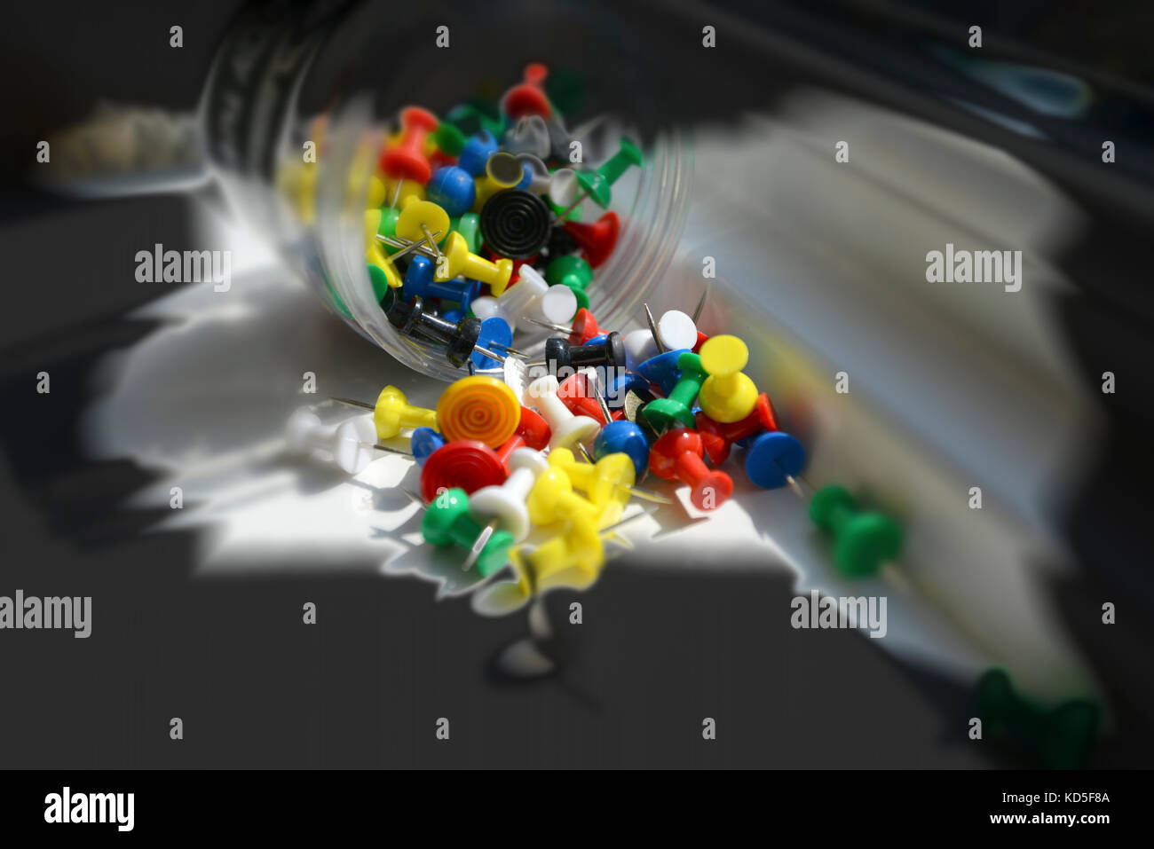 Studio shot - Plastic container of primary coloured  push pins, tumbling, forming a colourful abstract splash. Background copy space Stock Photo