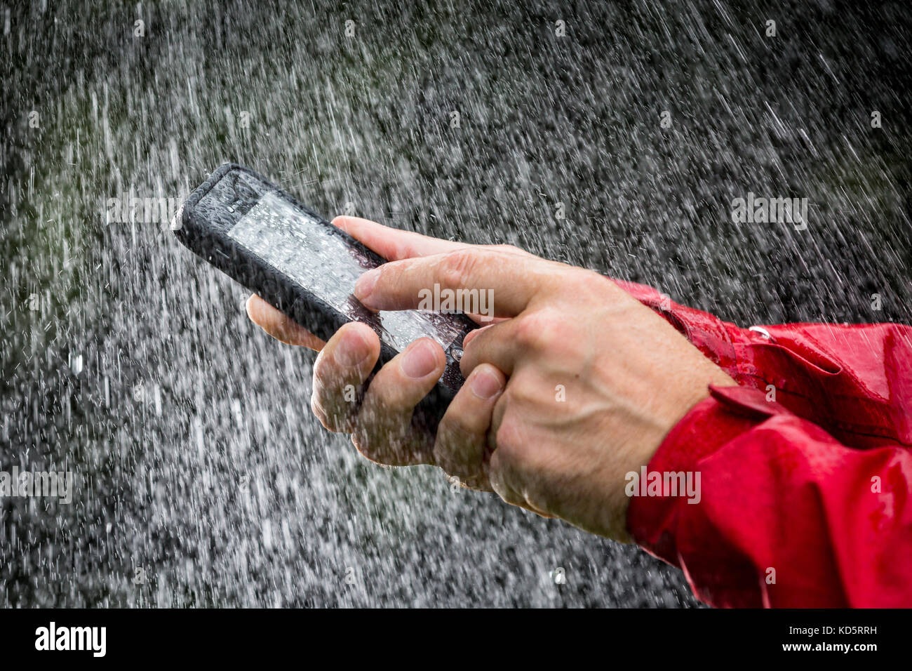 A man using a mobile phone in a waterproof case outside in the rain Stock Photo