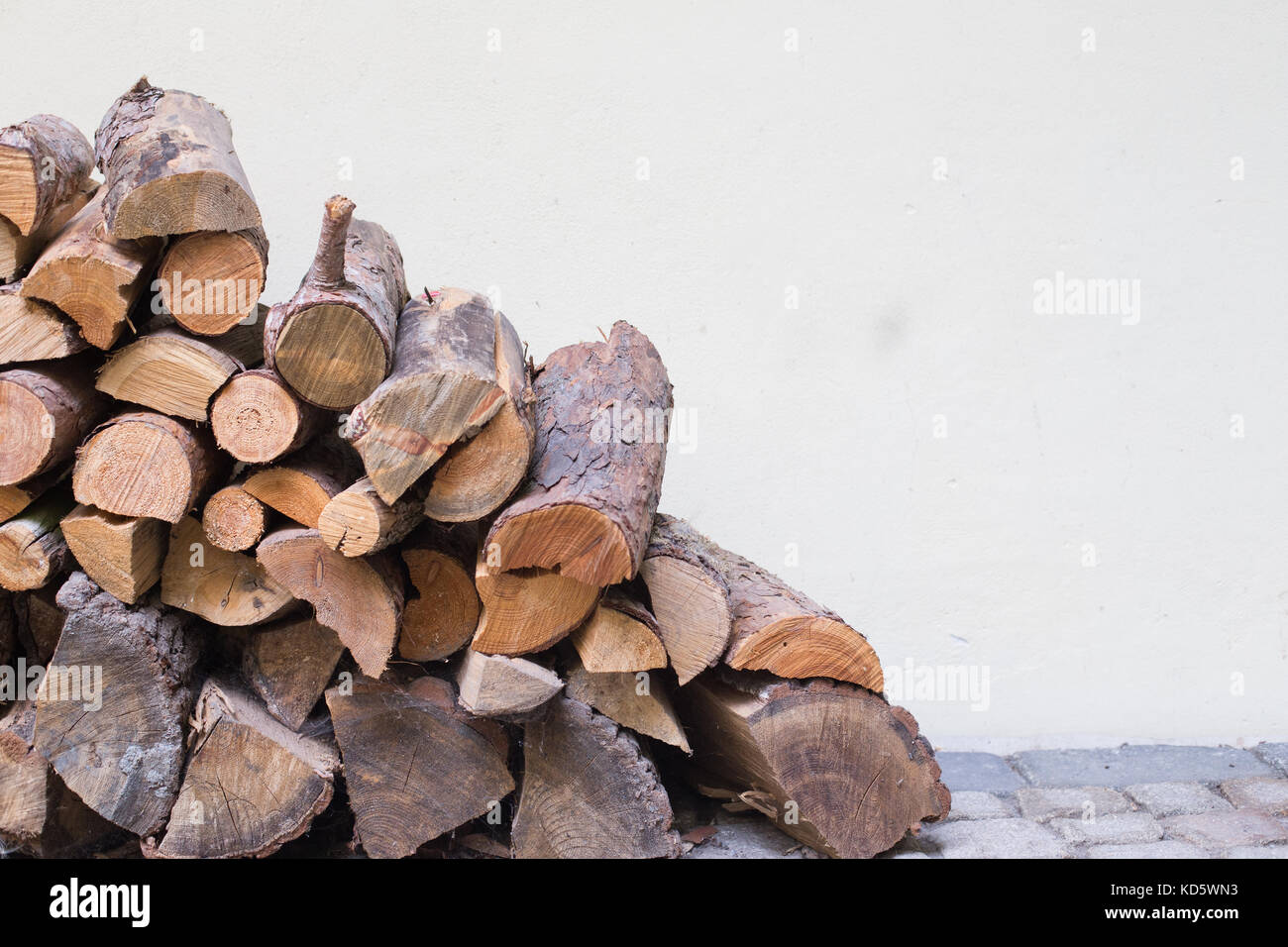 Fire Wood Pile on the floor outside a white wall , outdoor Woodshed , fall winter background , Cut tree trunks Stock Photo