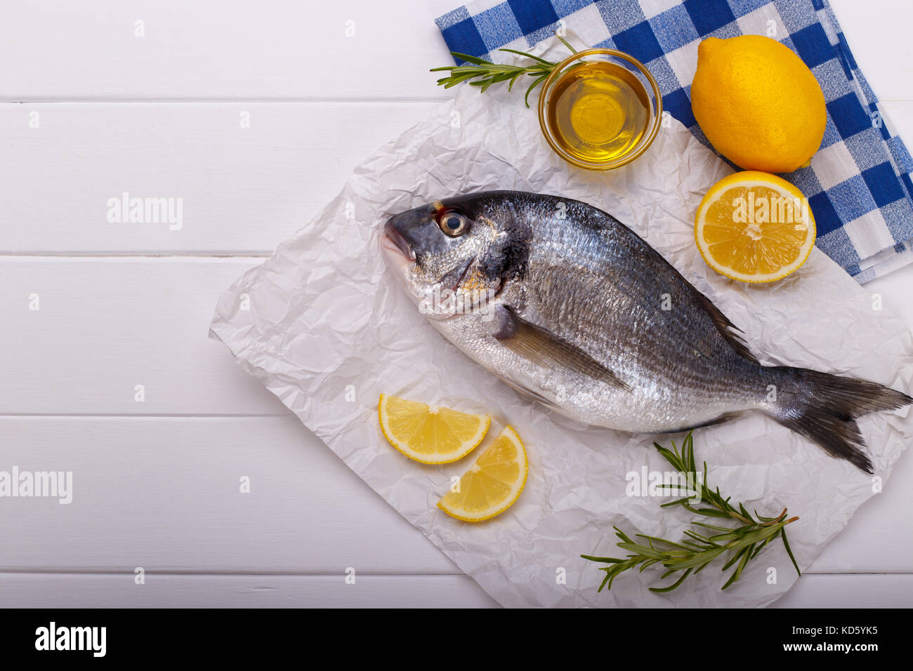 Fresh raw sea bream fish with lemon slices, salt, rosemary and olive ...