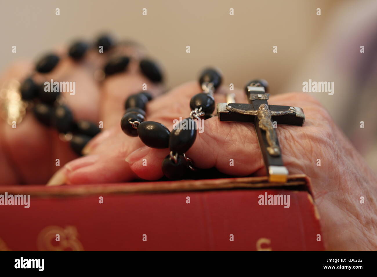 An elderly woman praying the rosary on top of her bible Stock Photo