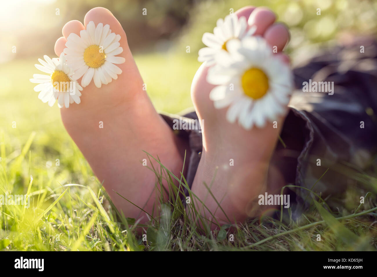Child with daisy between toes lying in meadow relaxing in summer sunshine Stock Photo