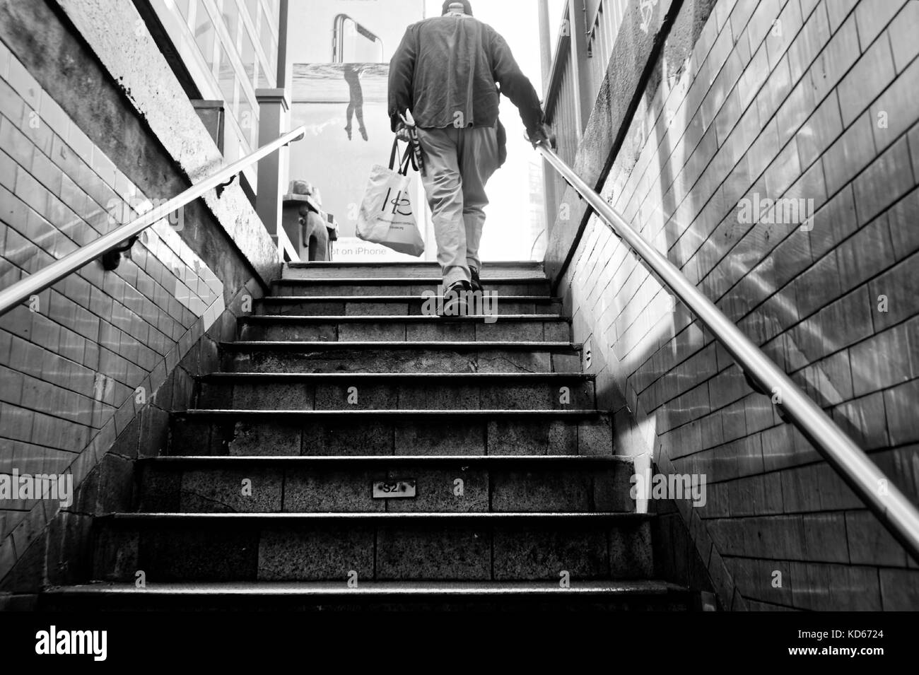 Older man walking up the subway steps with a shopping bag. Stock Photo