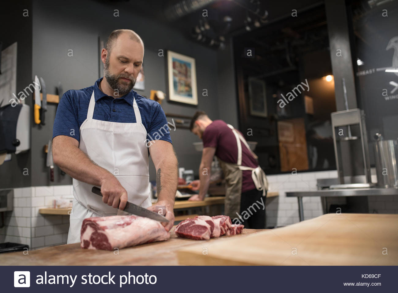 Male butcher with knife cutting into raw red meat in butcher Stock