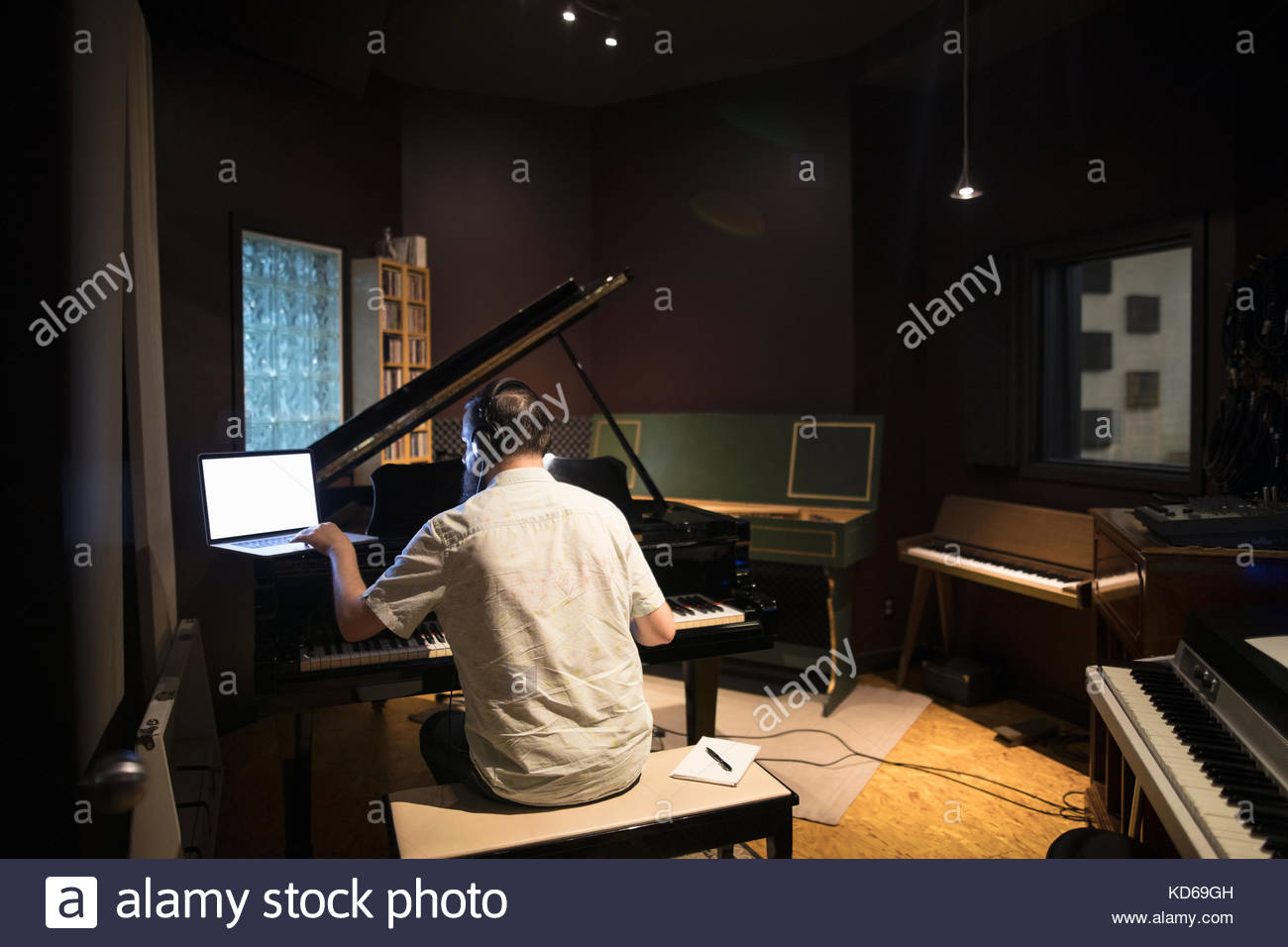 Male pianist playing grand piano, writing music at laptop in recording studio Stock Photo