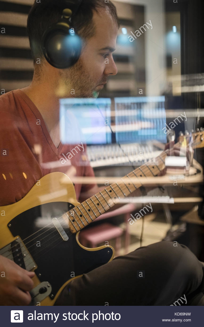 Focused male guitarist with headphones playing in recording studio