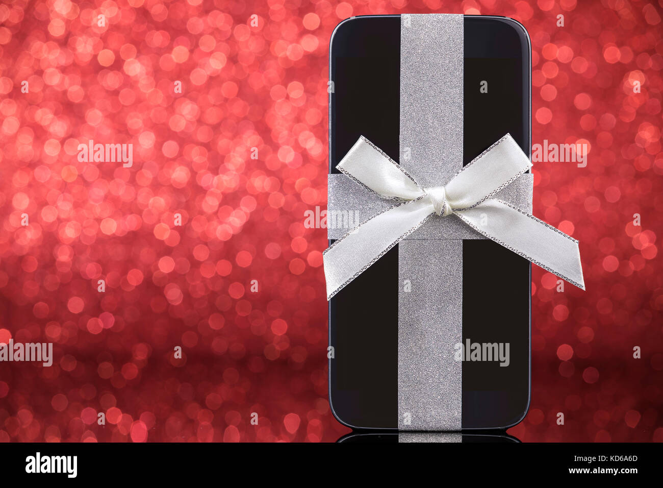 Smartphone for Christmas gift on black glass table over red background. Focus on smartphone. Stock Photo