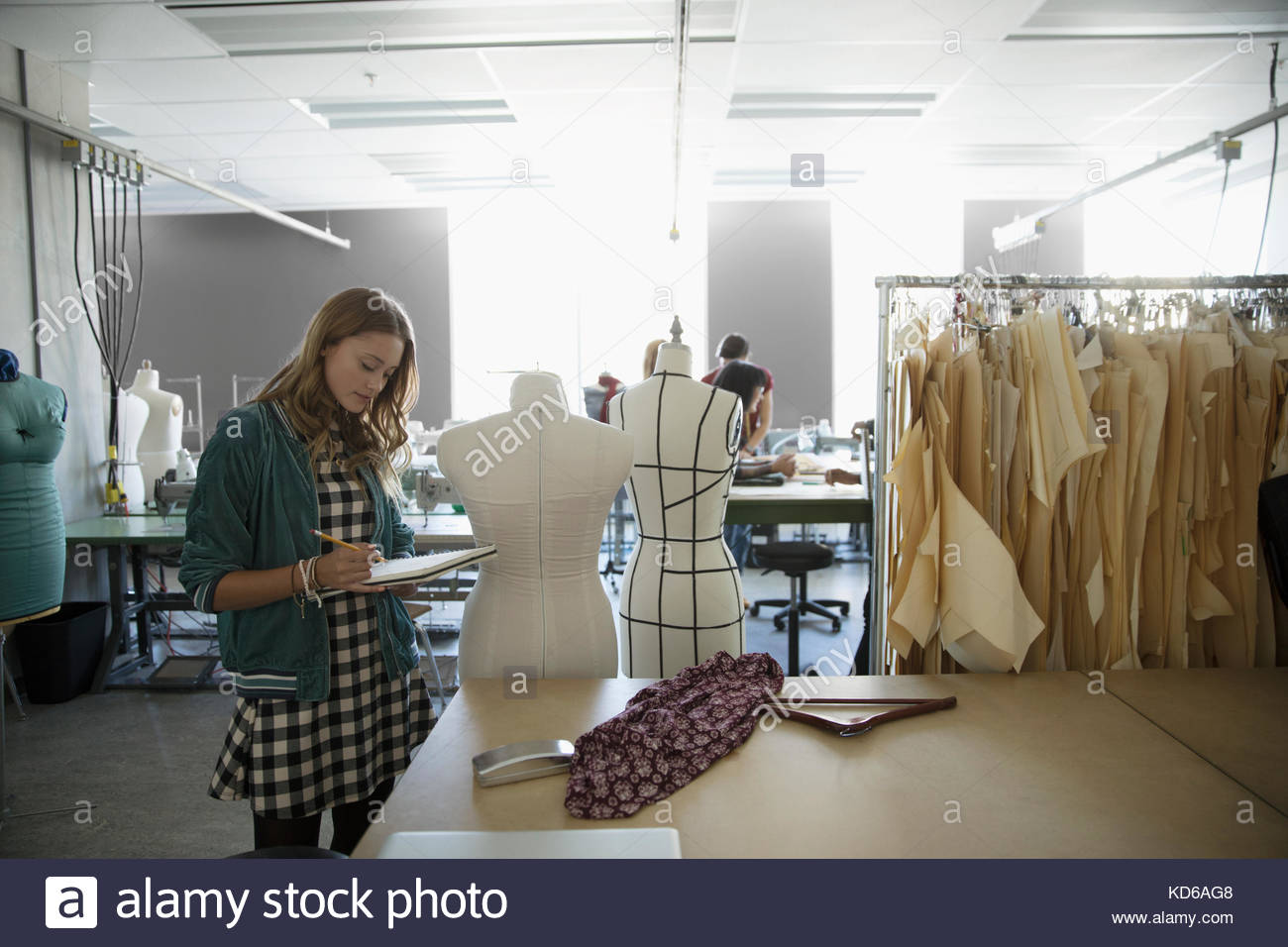 Female fashion design student sketching in notebook at dressmakers