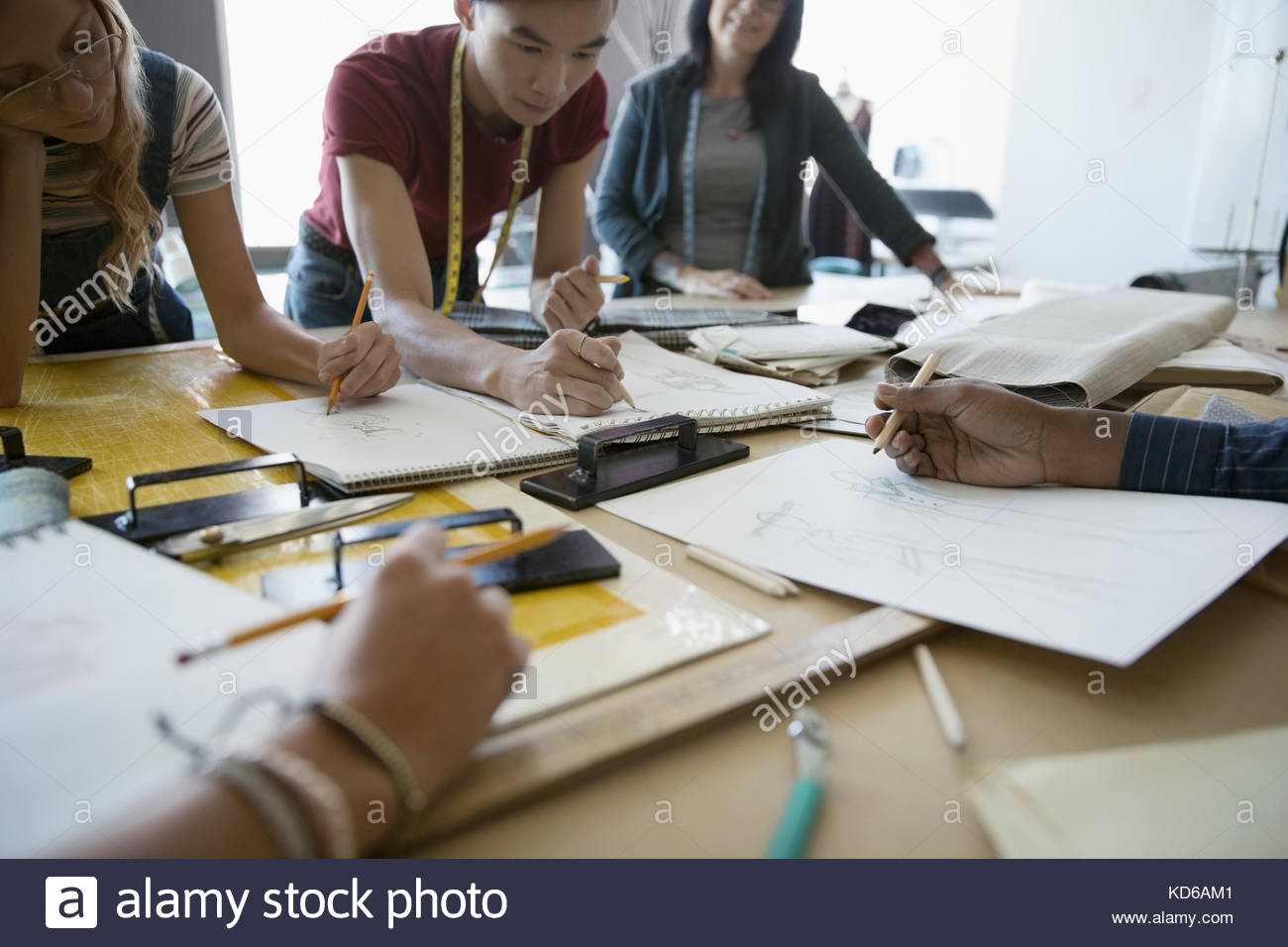 Fashion design students talking, sketching at workbench in studio Stock Photo