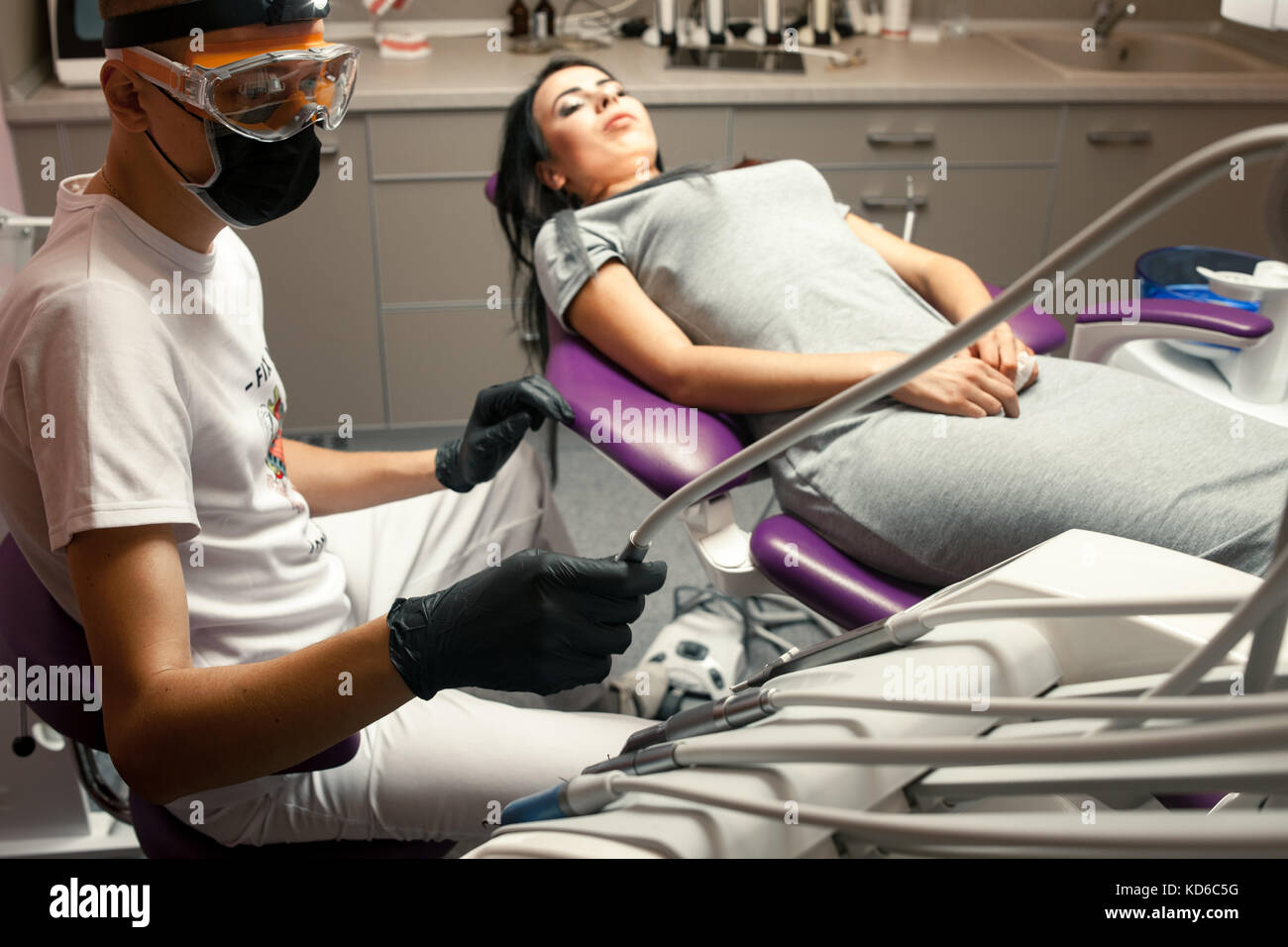 Young woman treats teeth in dental office. Male dentist in gloves,  protective glasses and mask takes dental drill Stock Photo - Alamy