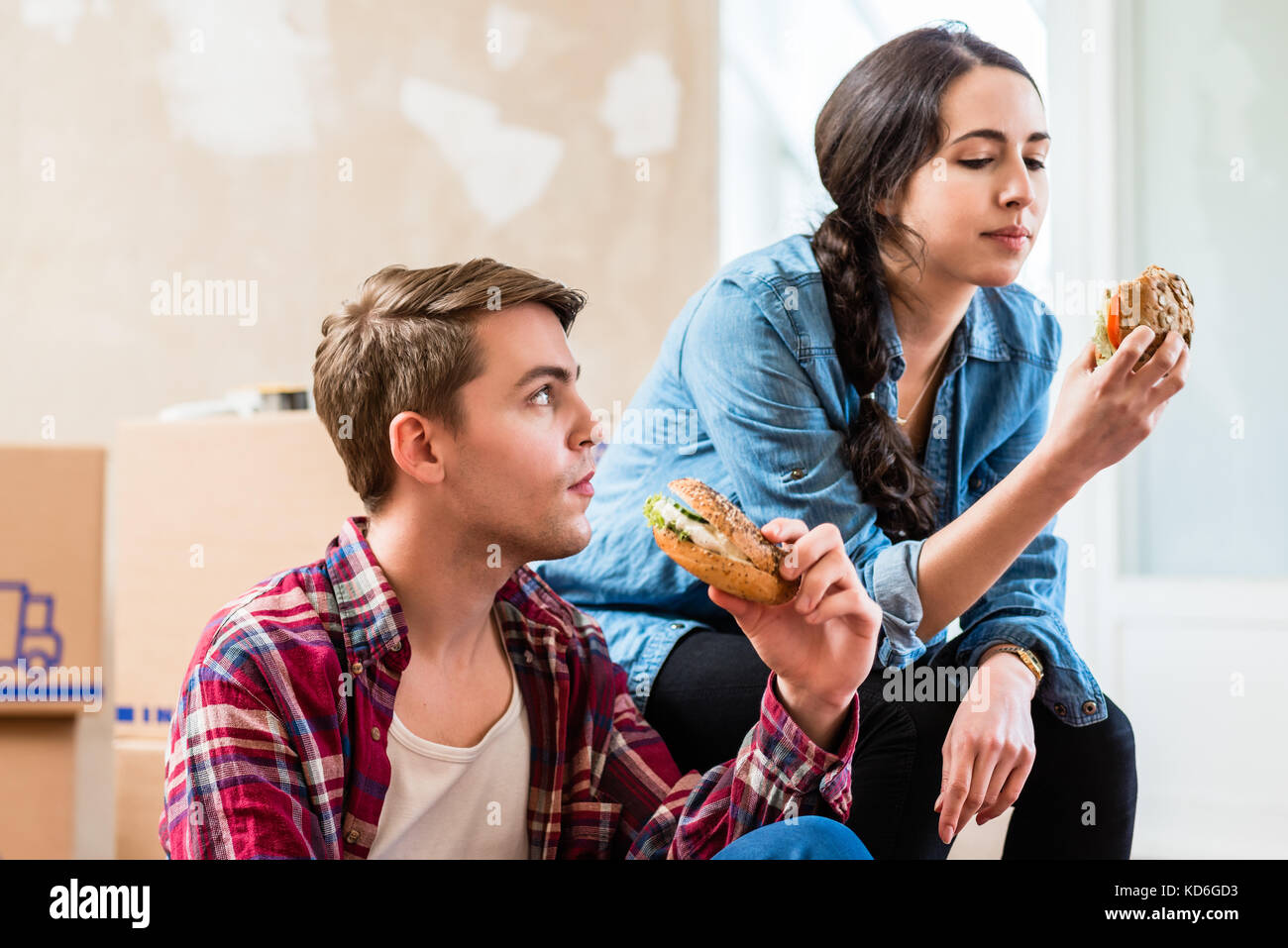 Young couple looking tired while eating a sandwich during break  Stock Photo