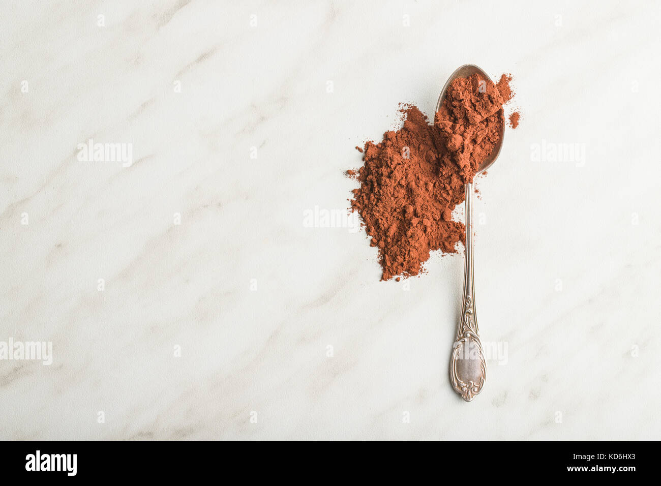 Dark cocoa powder in spoon on white table. Top view. Stock Photo