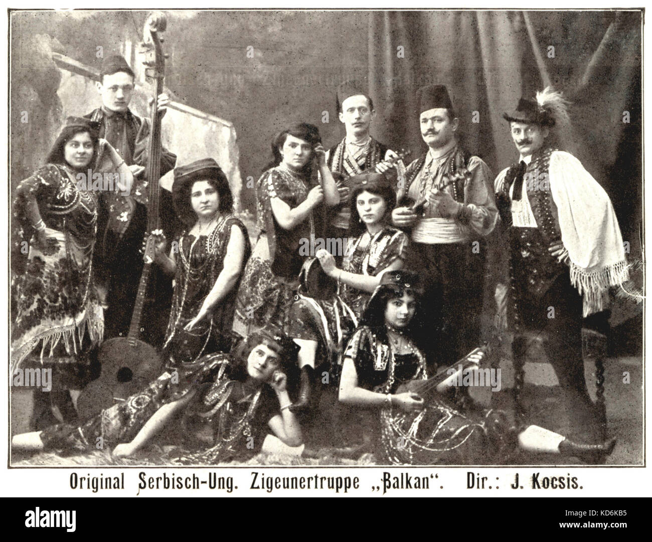 Serbian-Hungarian gypsy band, 'Balkan'. Men and women in traditional costume. Conductor: J. Kocsis. Double-bass, tambourine, guitar  and other stringed-instruments. Early 20th century postcard. Stock Photo