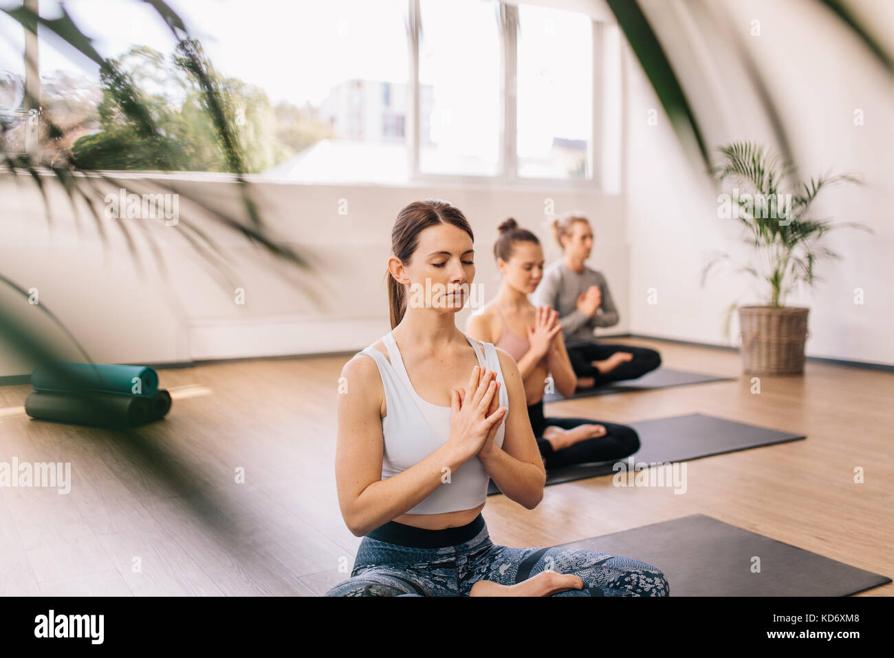 Fitness people sitting on floor with legs crossed and hands joined. Group of young people meditating in lotus pose at yoga class. Stock Photo