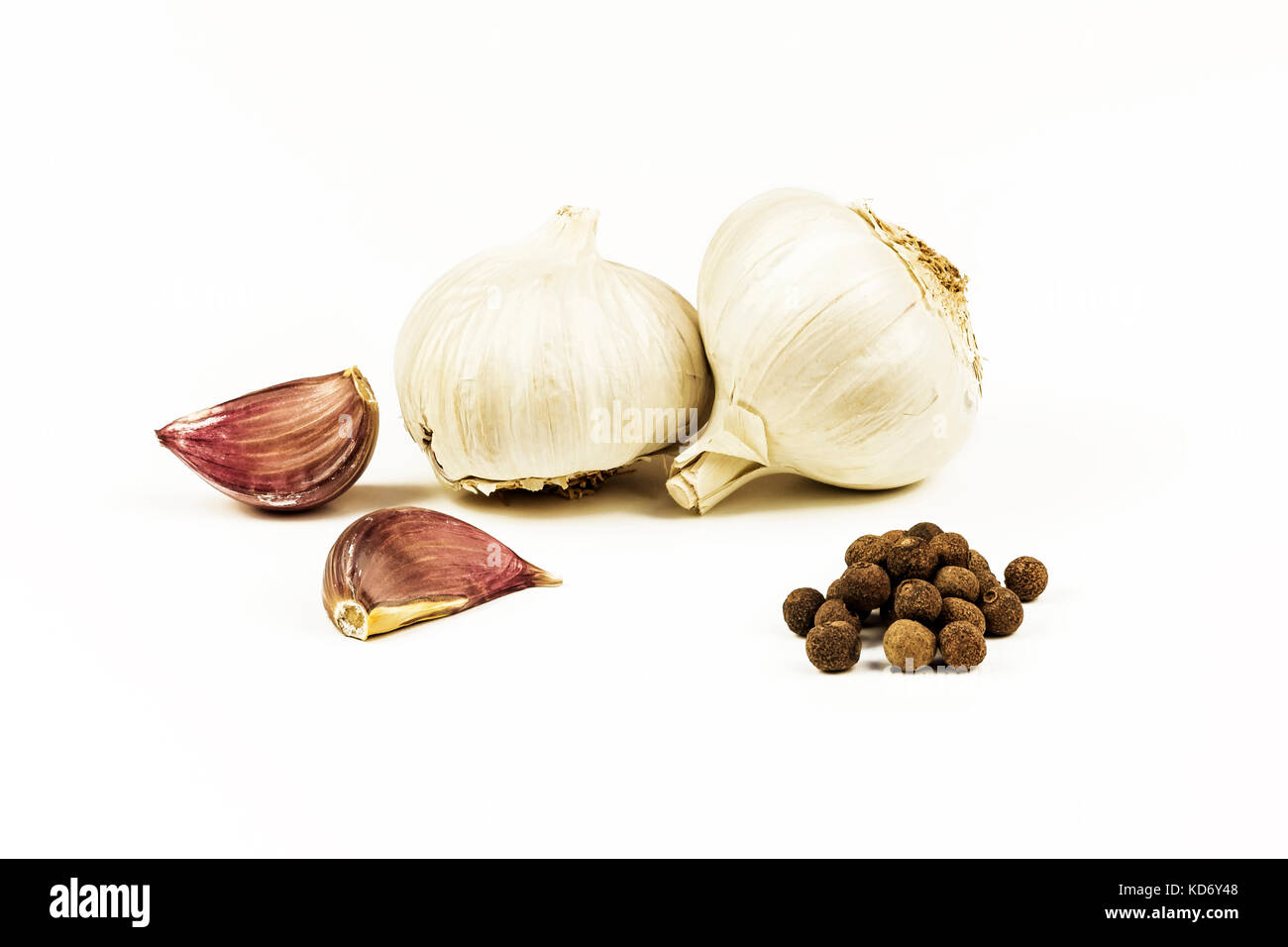 On a white background lie heads and uncooked cloves of garlic with peppercorns Stock Photo