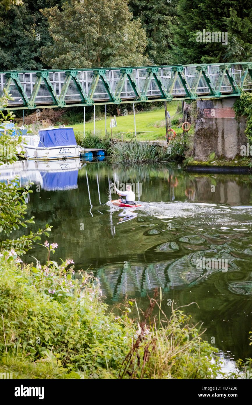 A canoeist paddles under Barming footbridge, his paddles make patterns in the still water of the River Medway, Kent, UK Stock Photo