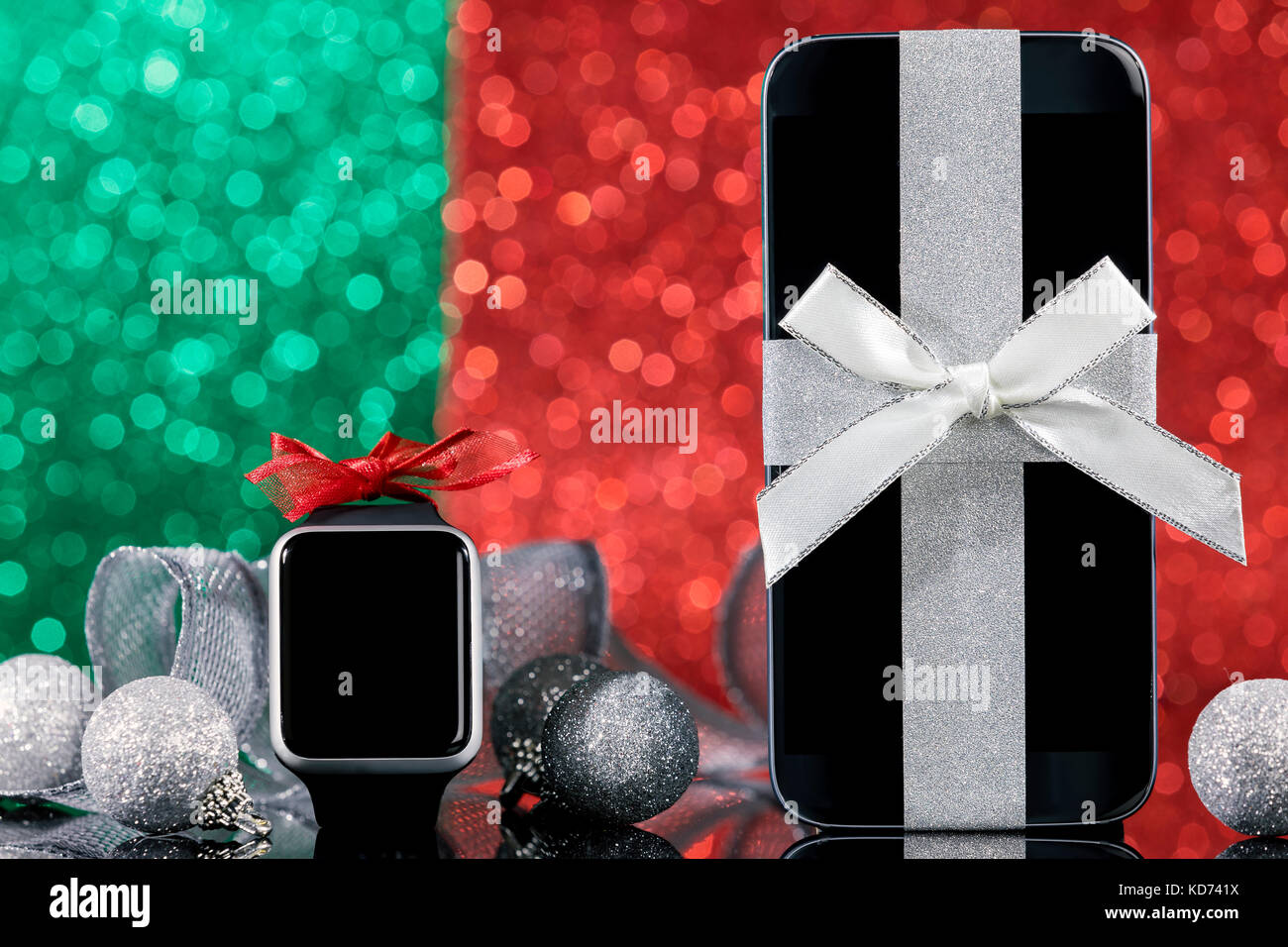 Smartphone and smartwatch and decorations for Christmas tree on black glass table over green and red background. Focus on smartphone. Stock Photo