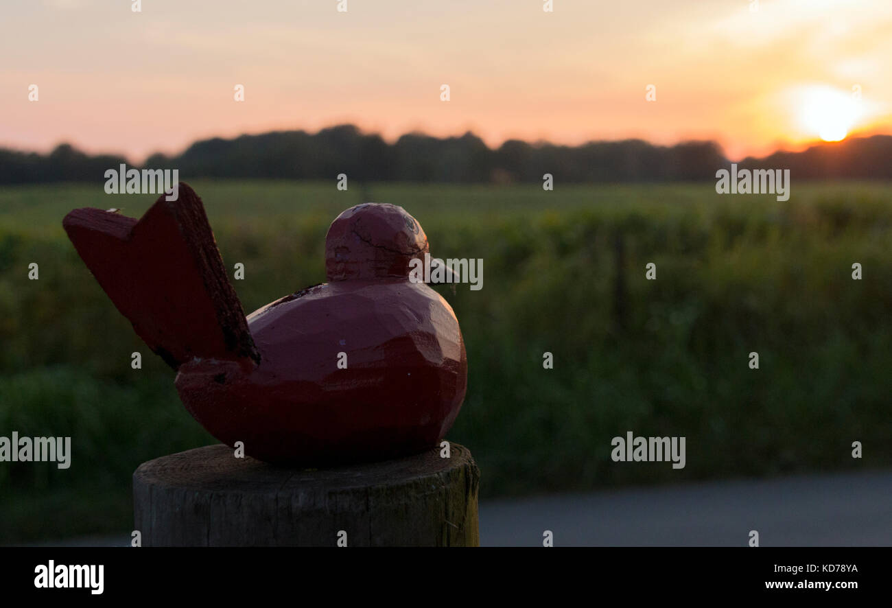 A wood carving of a bird sits on a post in rural Kentucky during sunset. Stock Photo