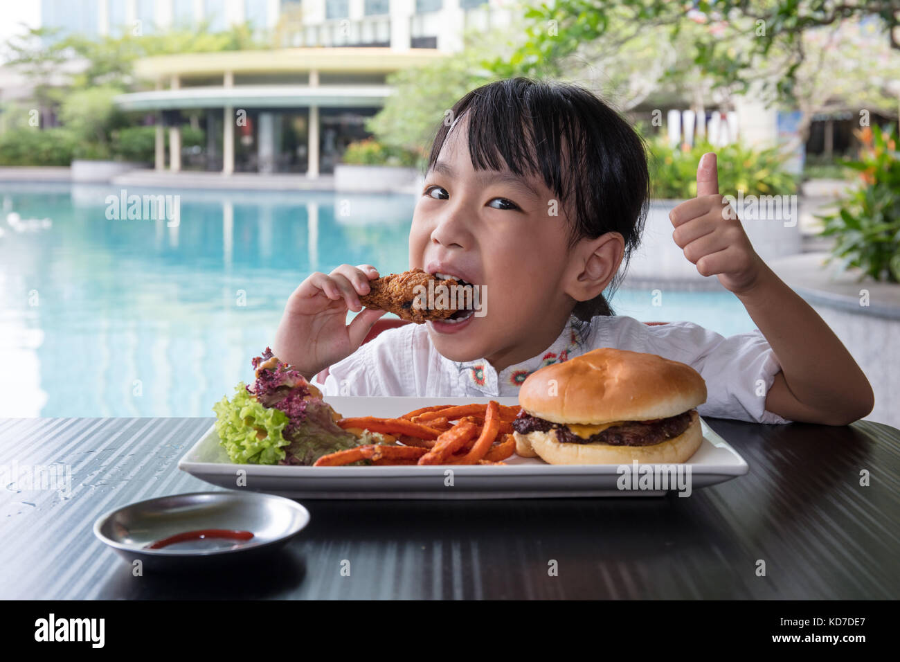 Asian Little Chinese Girl Eating Burger and Fried chicken at Outdoor Cafe Stock Photo