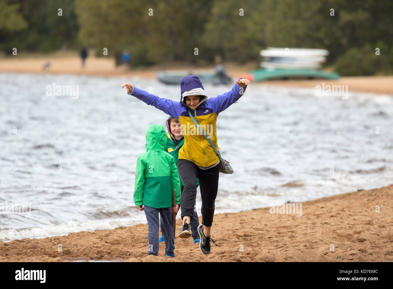 Cairngorms, UK.  The day started off with clear blue sky but a weather front from the west started to creep into the Highlands mid-afternoon. Walkers on the shore of Loch Morlich dressed for the cooler weather as they jump over a small streem that enters the loch. Stock Photo
