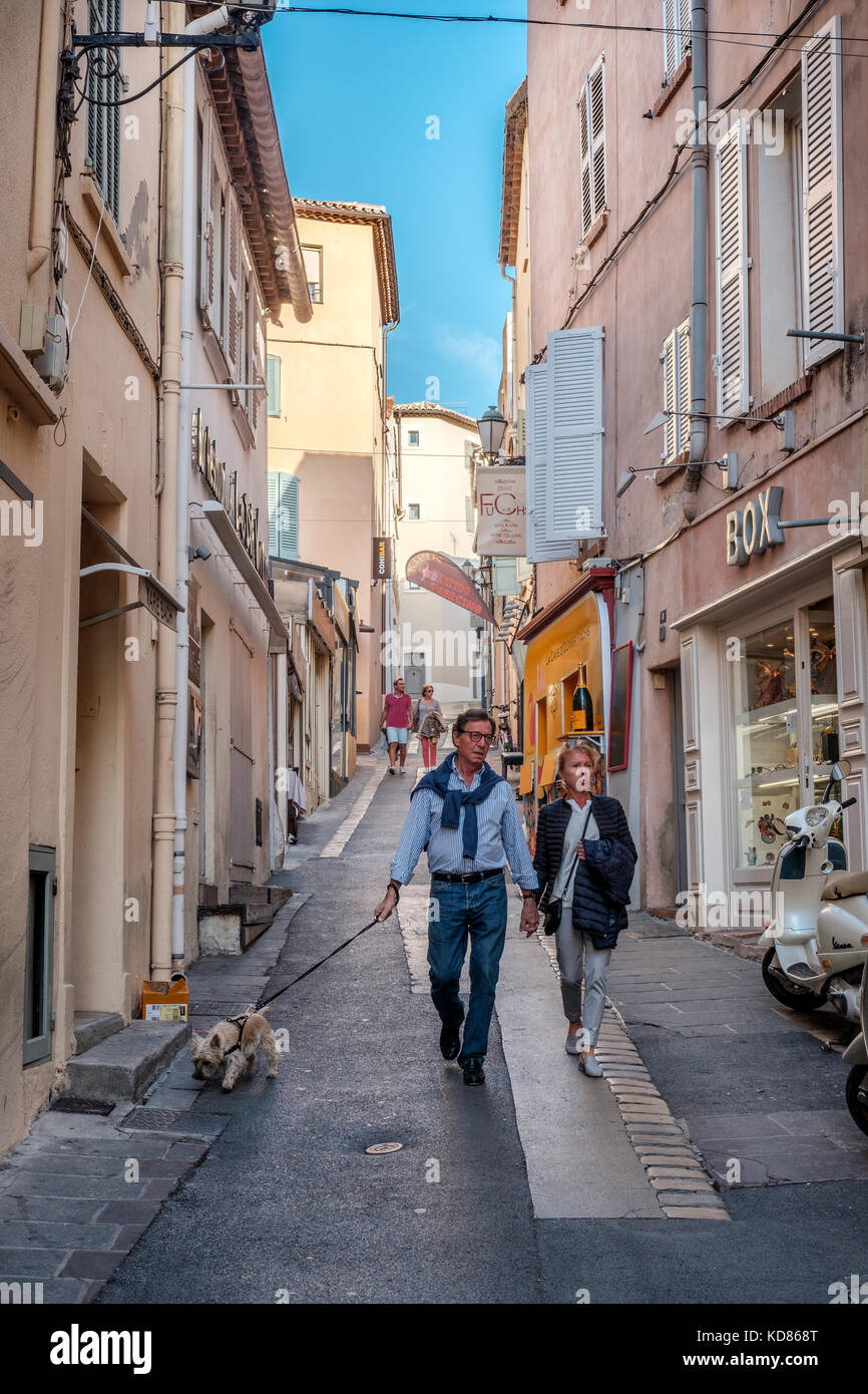 Saint Tropez street scene.  Couple with a dog walk down a side street in Saint Tropez, France. Stock Photo