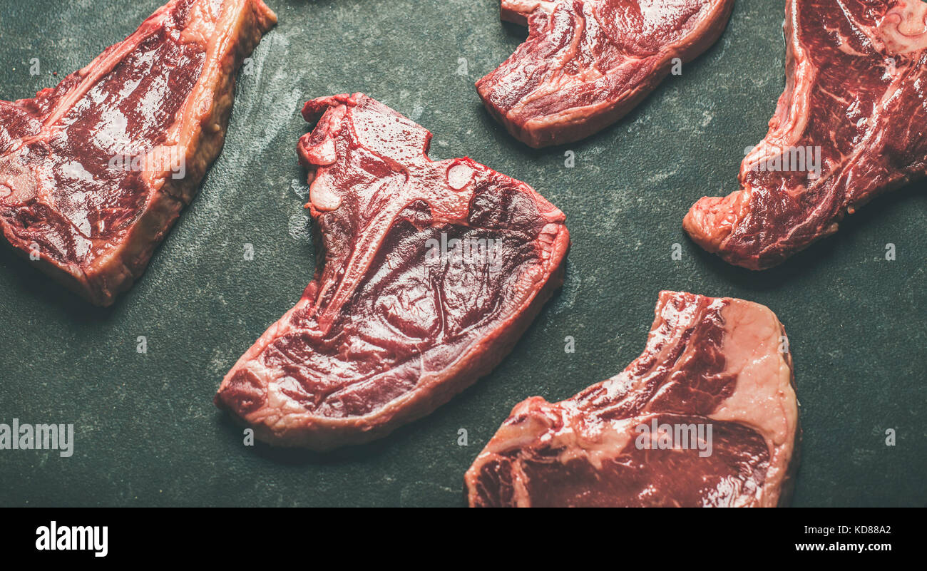 Fresh raw beef meat steak cuts over black stone background, selective focus. Porterhouse, t-bone and rib-eye steaks. Butcher' s shop or cooking meat d Stock Photo