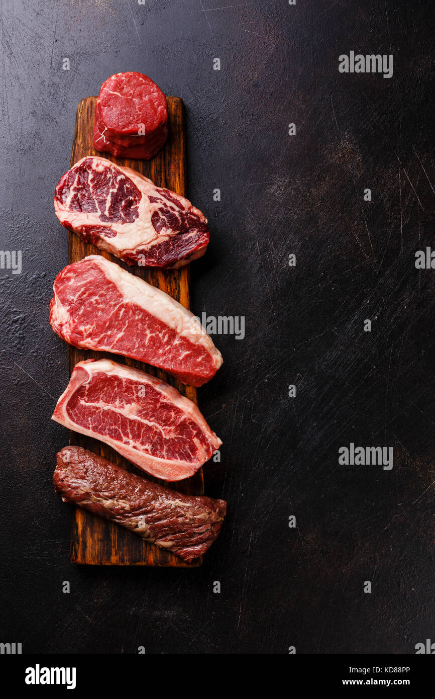 Variety of Raw Black Angus Prime meat steaks Machete, Blade on bone, Striploin, Rib eye, Tenderloin fillet mignon on dark background copy space Stock Photo