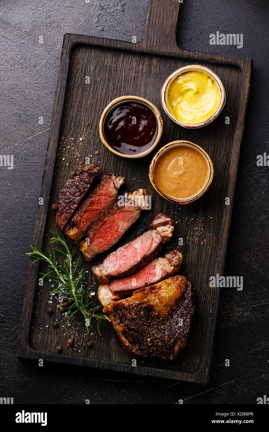Sliced grilled Rib eye steak and three different sauces: Pepper sauce, Mustard and Barbecue on dark background Stock Photo