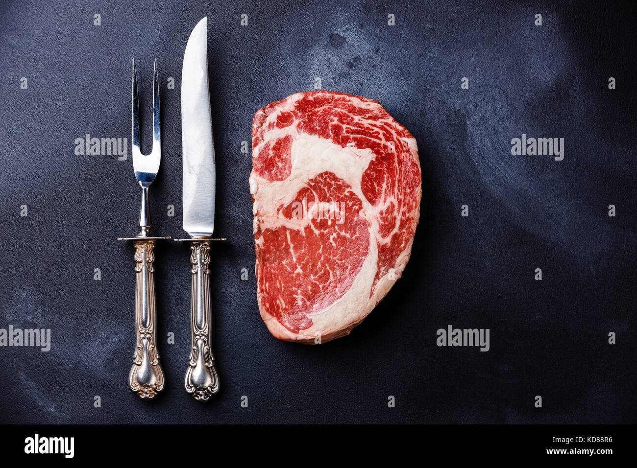 Raw fresh marbled meat Steak Rib eye Black Angus and fork and knife on dark background Stock Photo