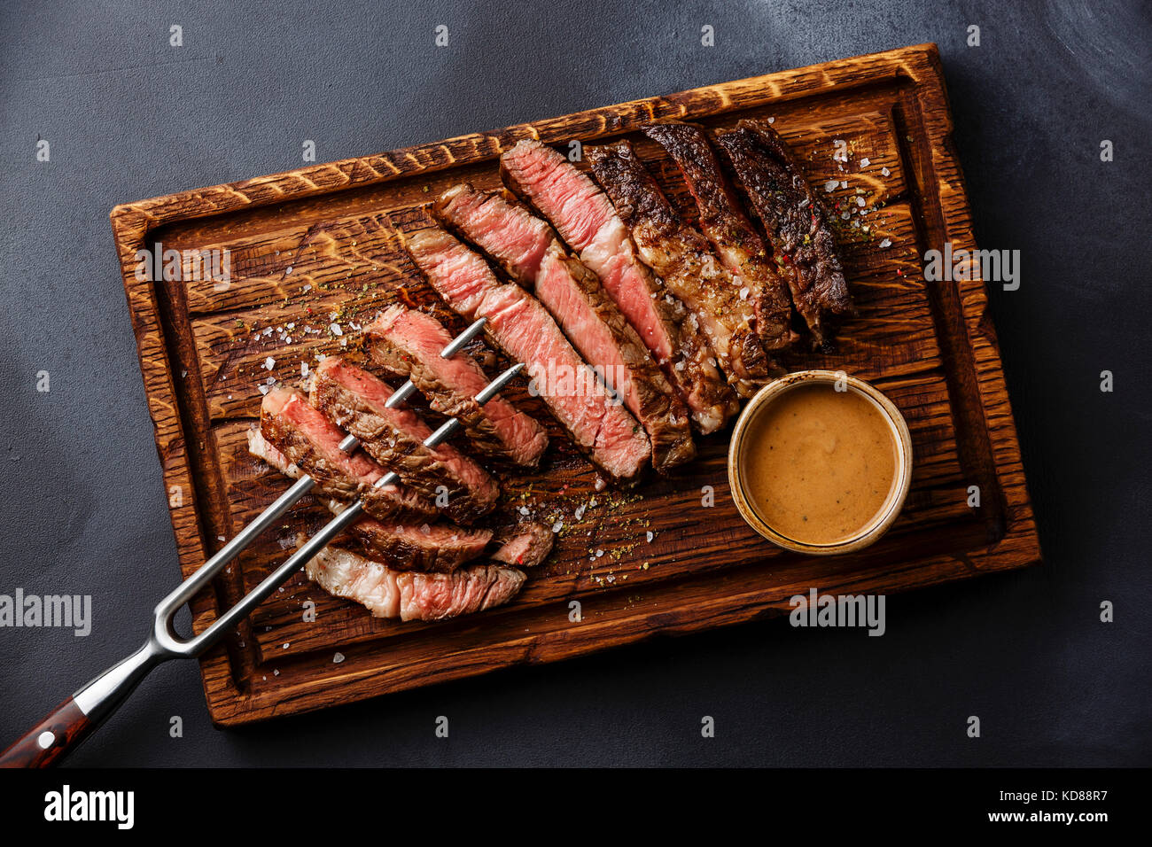 Sliced grilled meat steak Rib eye on meat fork and Pepper sauce on dark background Stock Photo