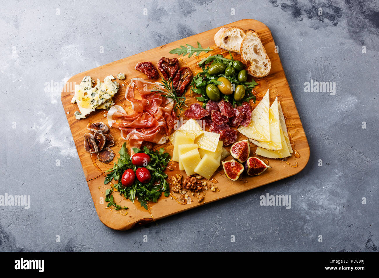 Italian snacks food with Ham, Olive, Cheese, Sun-dried tomatoes, Sausage and Bread on wooden cutting board on concrete background Stock Photo