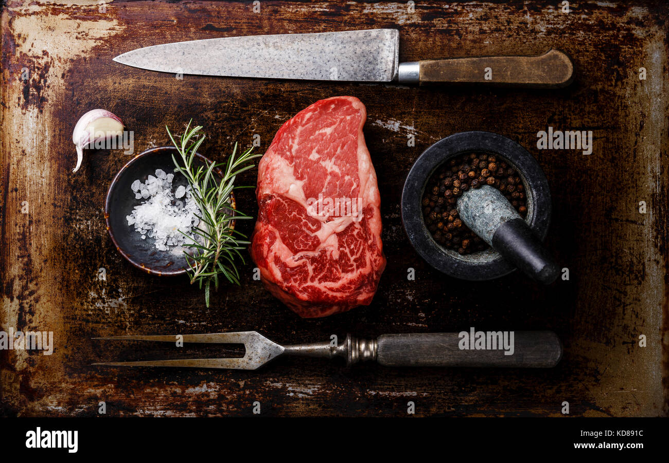 Raw fresh marbled meat Steak Rib eye Black Angus, seasoning and fork and knife on dark background Stock Photo