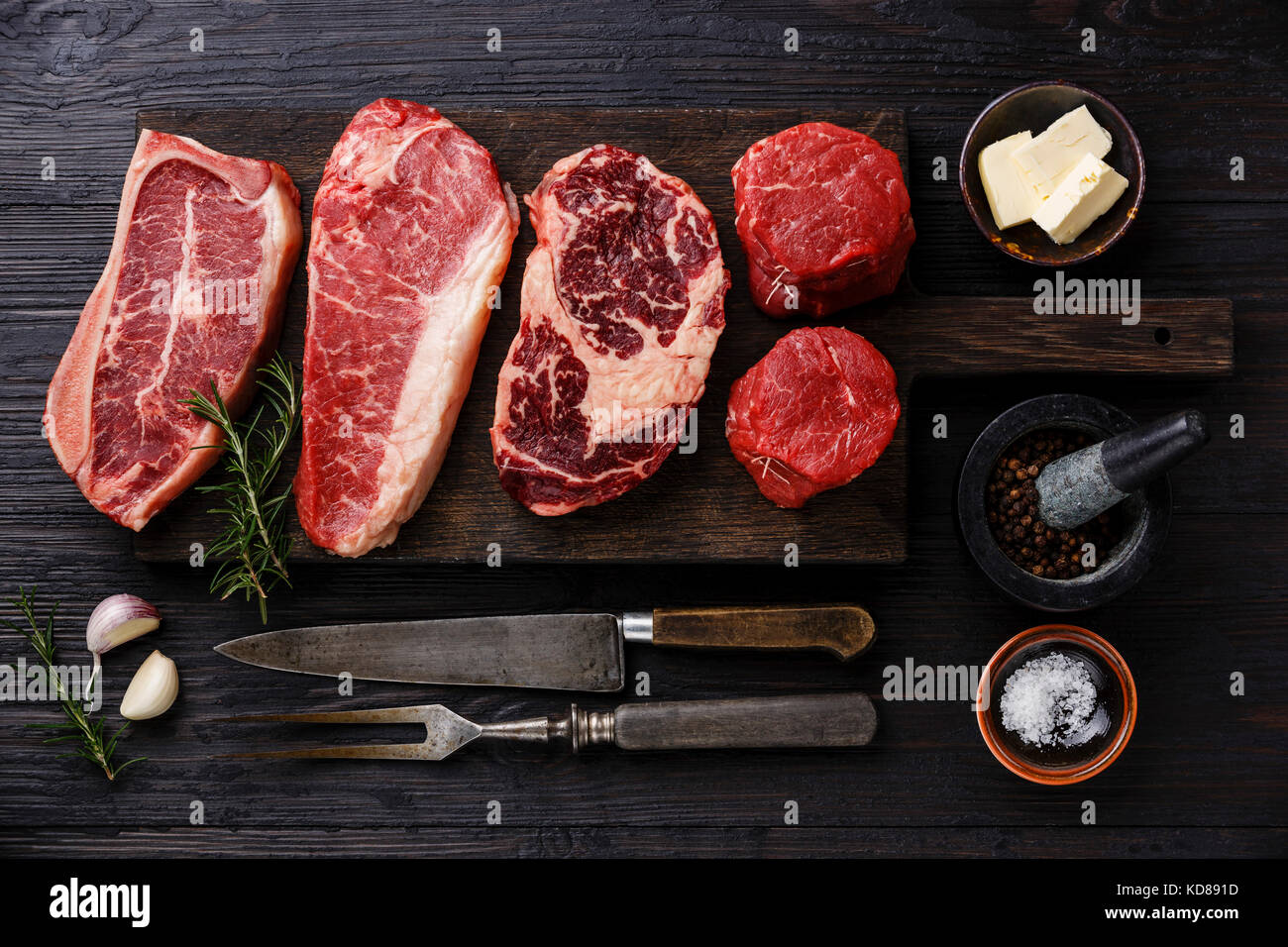 Variety of Raw Black Angus Prime meat steaks Blade on bone, Striploin, Rib eye, Tenderloin fillet mignon on wooden board and seasoning Stock Photo