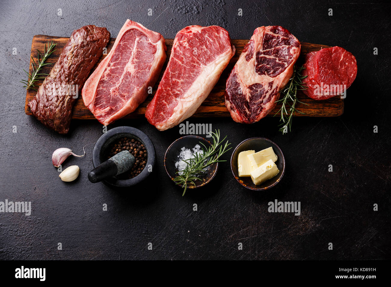 Variety of Raw Black Angus Prime meat steaks Machete, Blade on bone, Striploin, Rib eye, Tenderloin fillet mignon on wooden board and seasoning Stock Photo