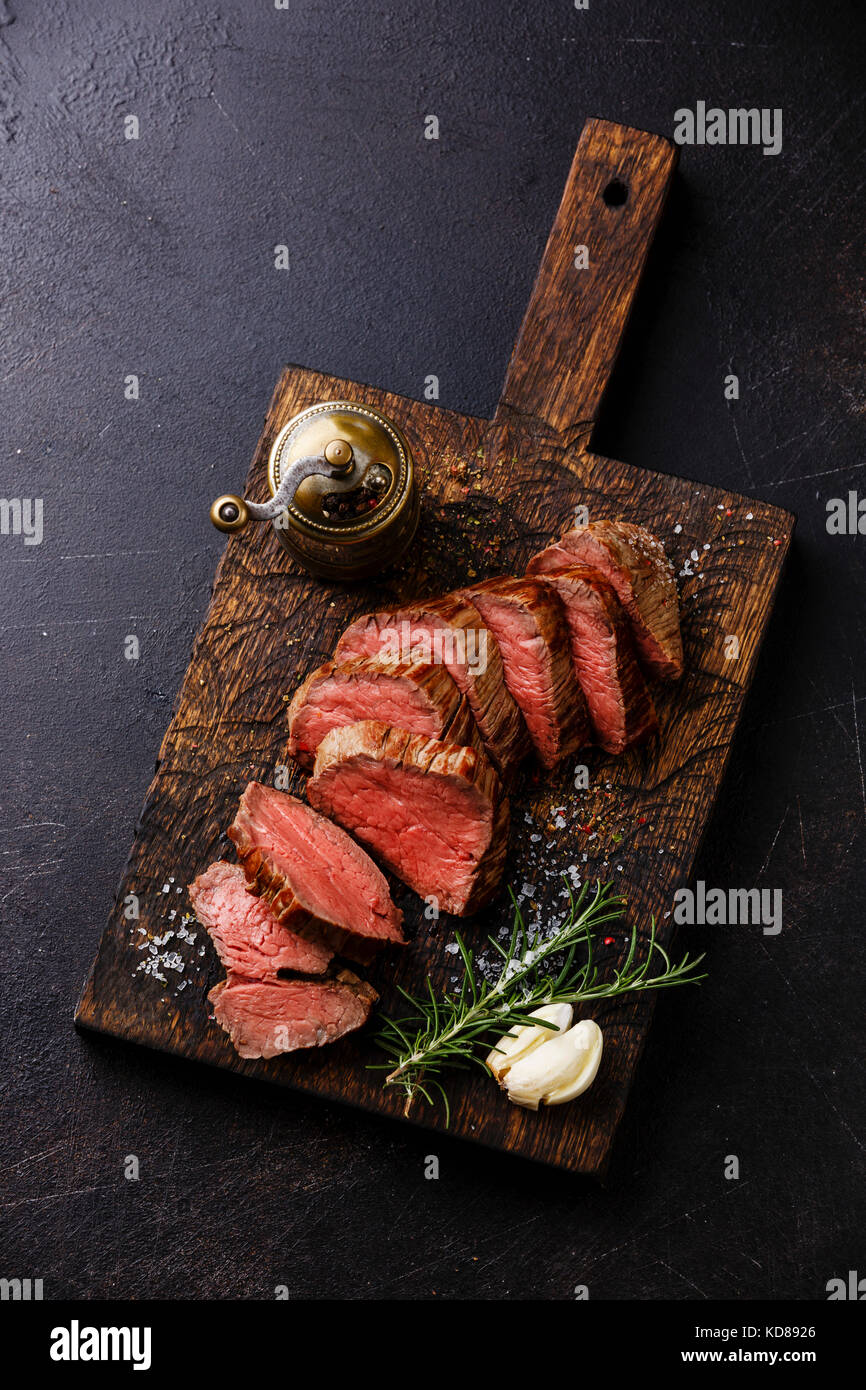 Sliced tenderloin Steak Roast beef on wooden cutting board on dark background Stock Photo