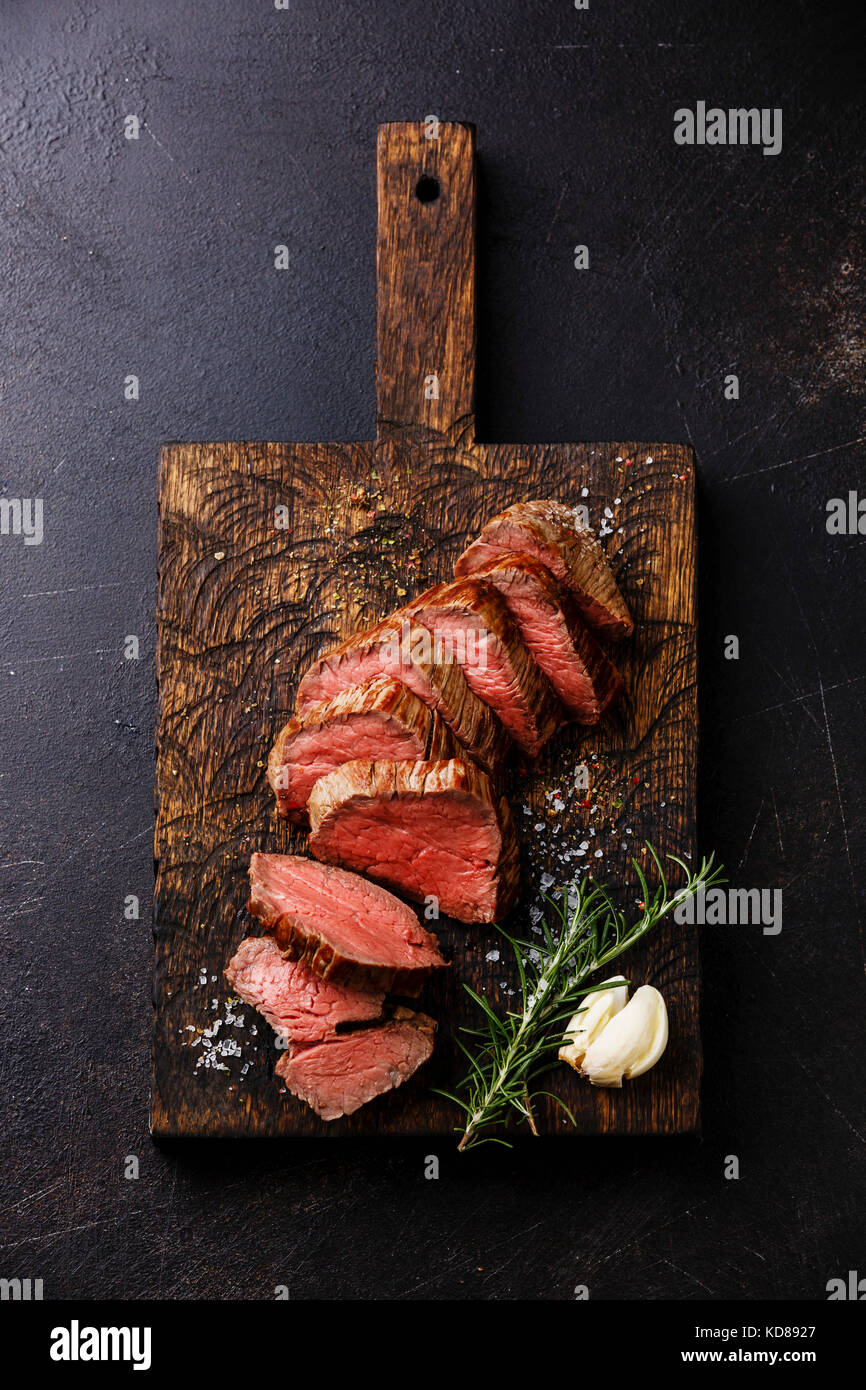 Sliced tenderloin Steak Roast beef on wooden cutting board on dark background Stock Photo