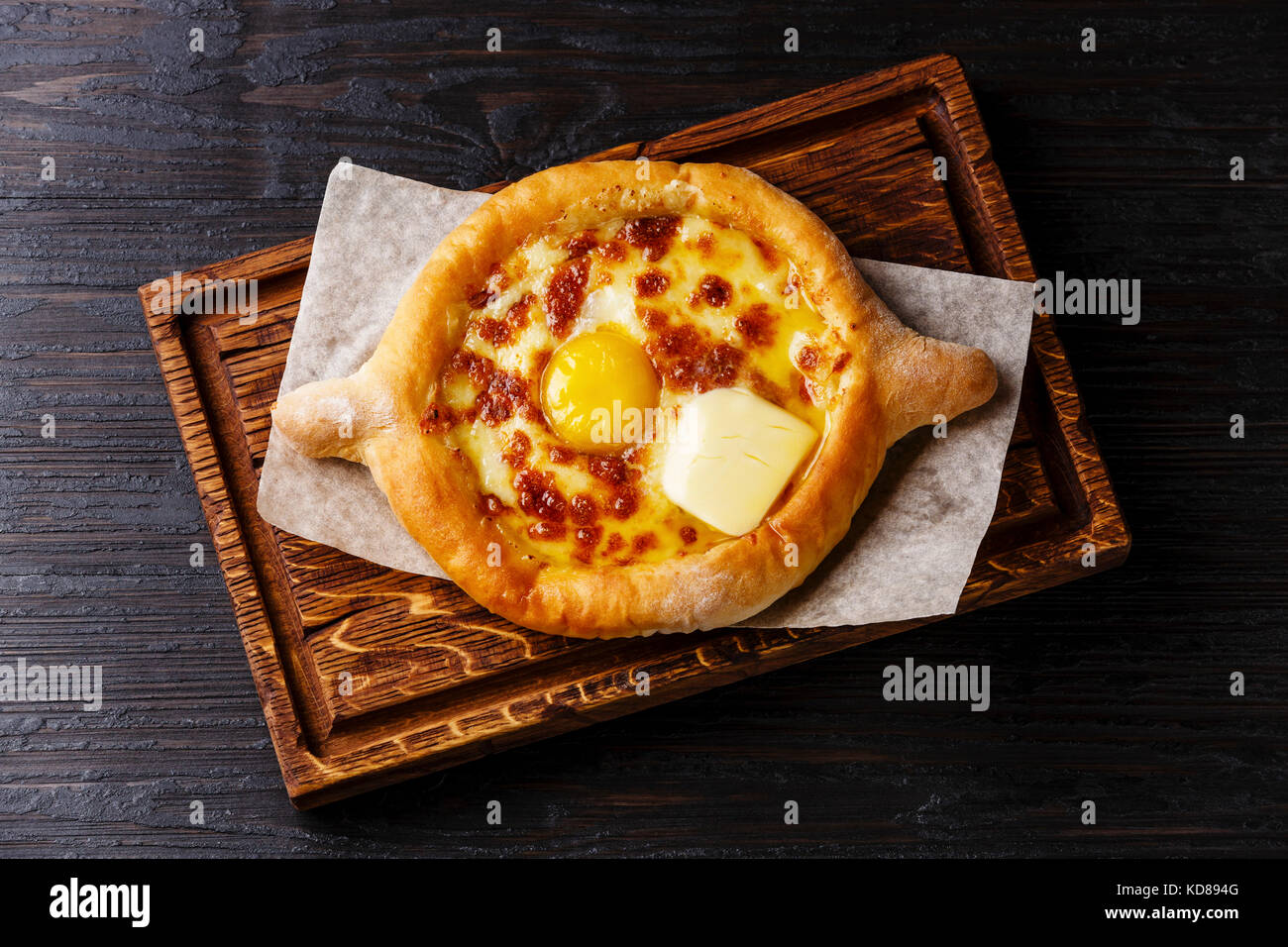Georgian cheese pastry Ajarian Khachapuri serving size on burned black wooden background Stock Photo