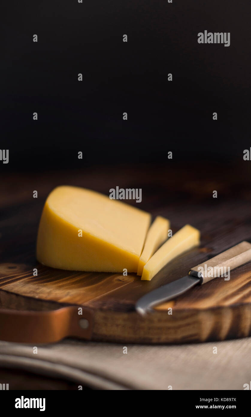 Wedge of smoked gouda cheese sliced on rustic wood cutting board with