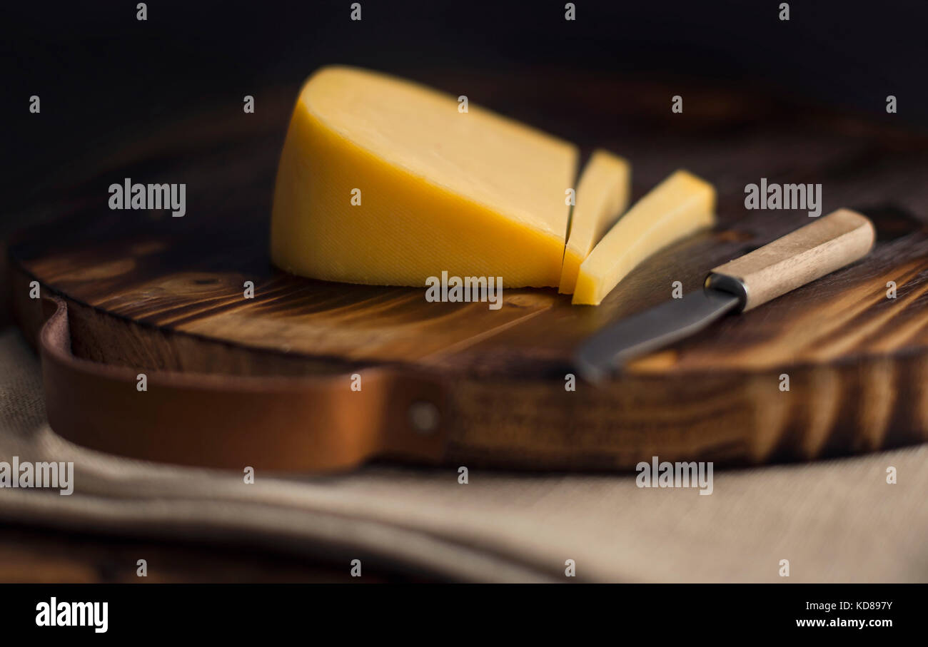 Large wedge of smoked gouda cheese sliced on rustic wood cutting board
