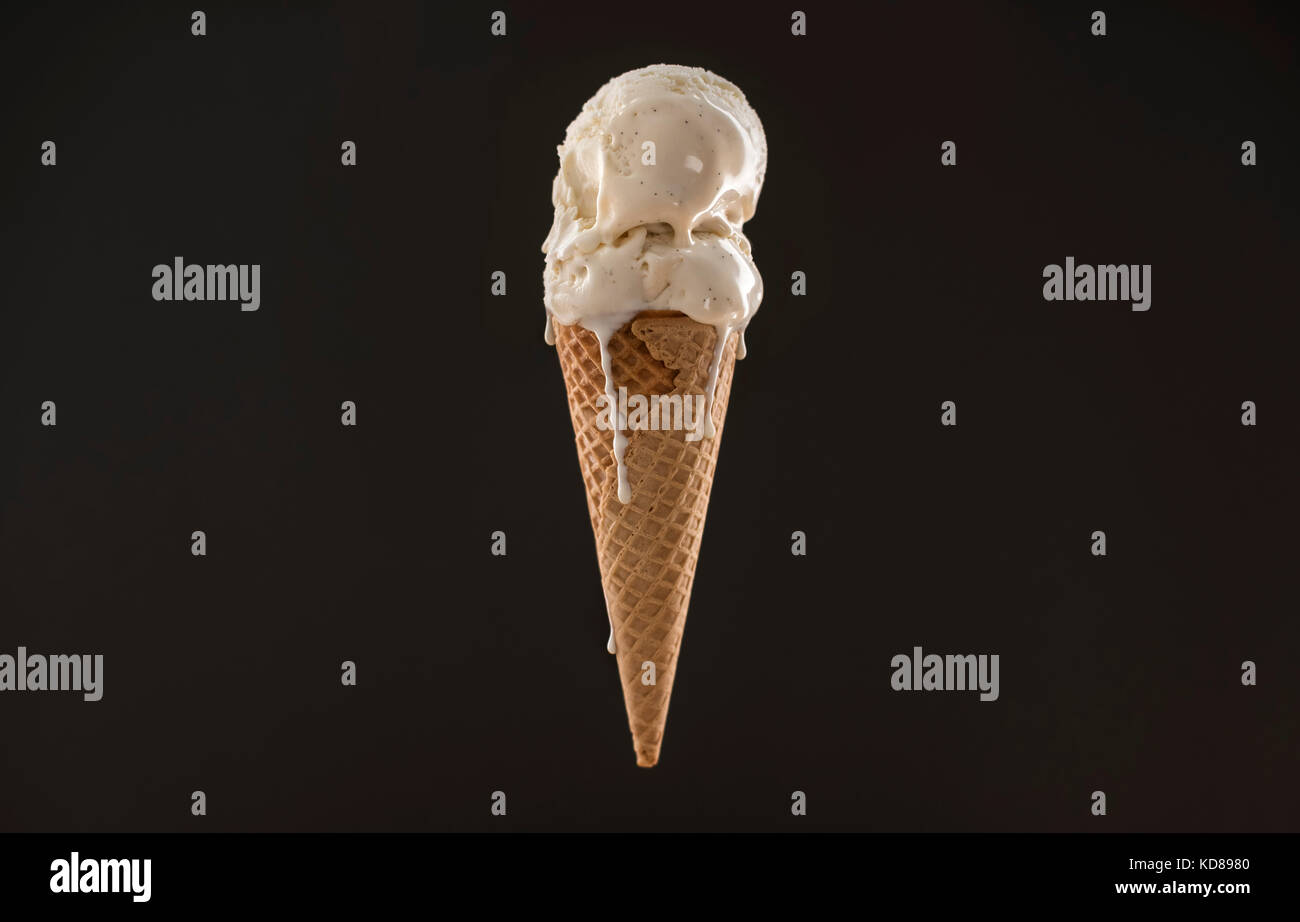 Melty vanilla ice cream scoops in a sugar cone floating on a dark gray surface. Stock Photo