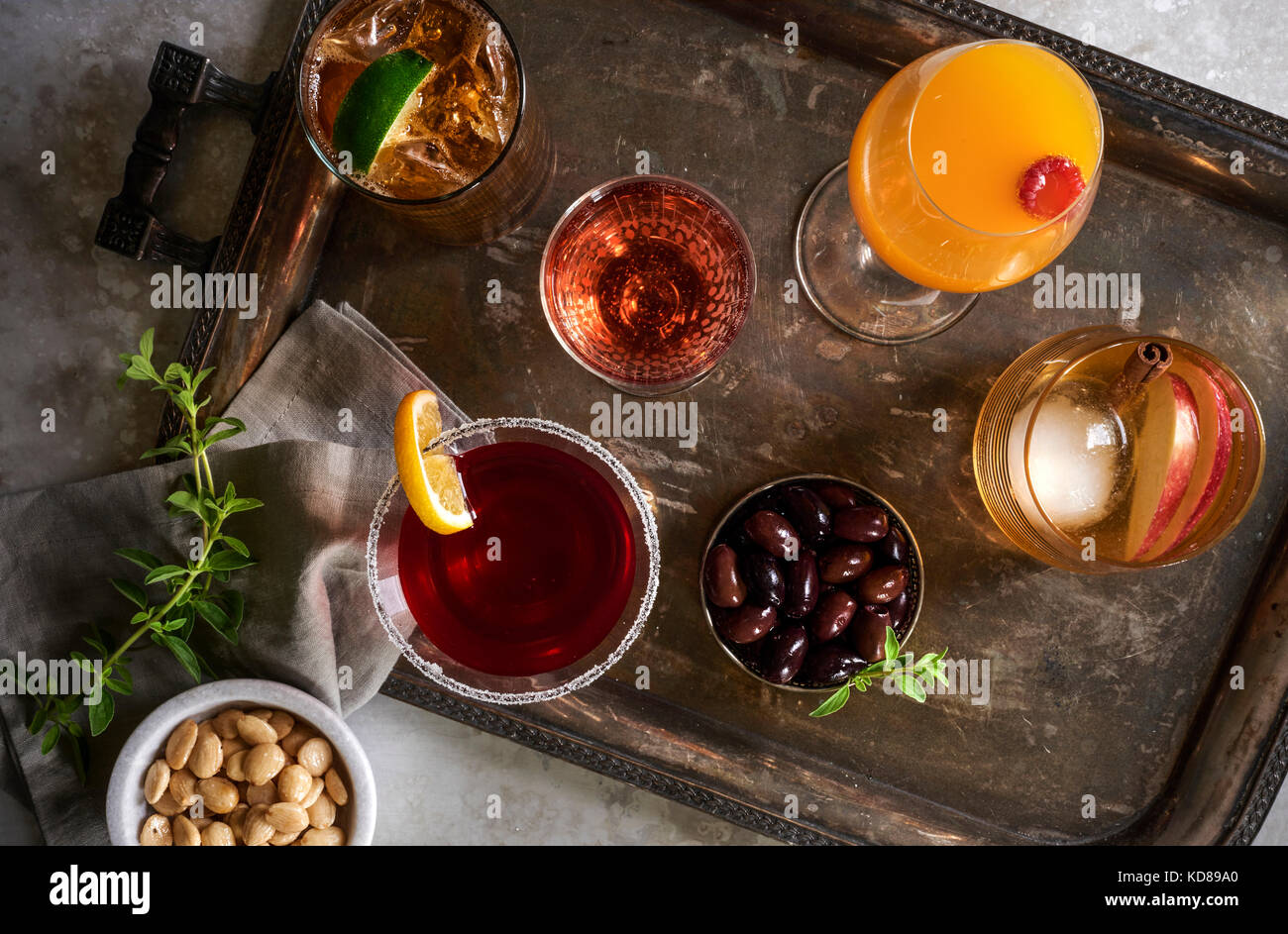 Rustic metal bar top with tray and multiple colorful cocktails. Garnished with fresh citrus wedges and fresh herbs. Stock Photo