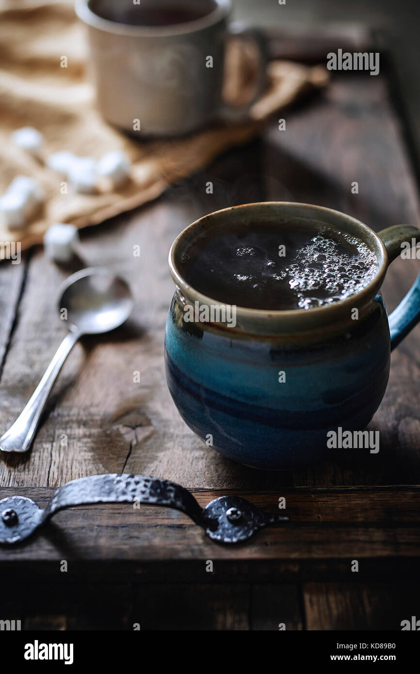 Handmade stone mug of steaming hot tea on rustic wood serving tray with morning light coming in behind. Stock Photo