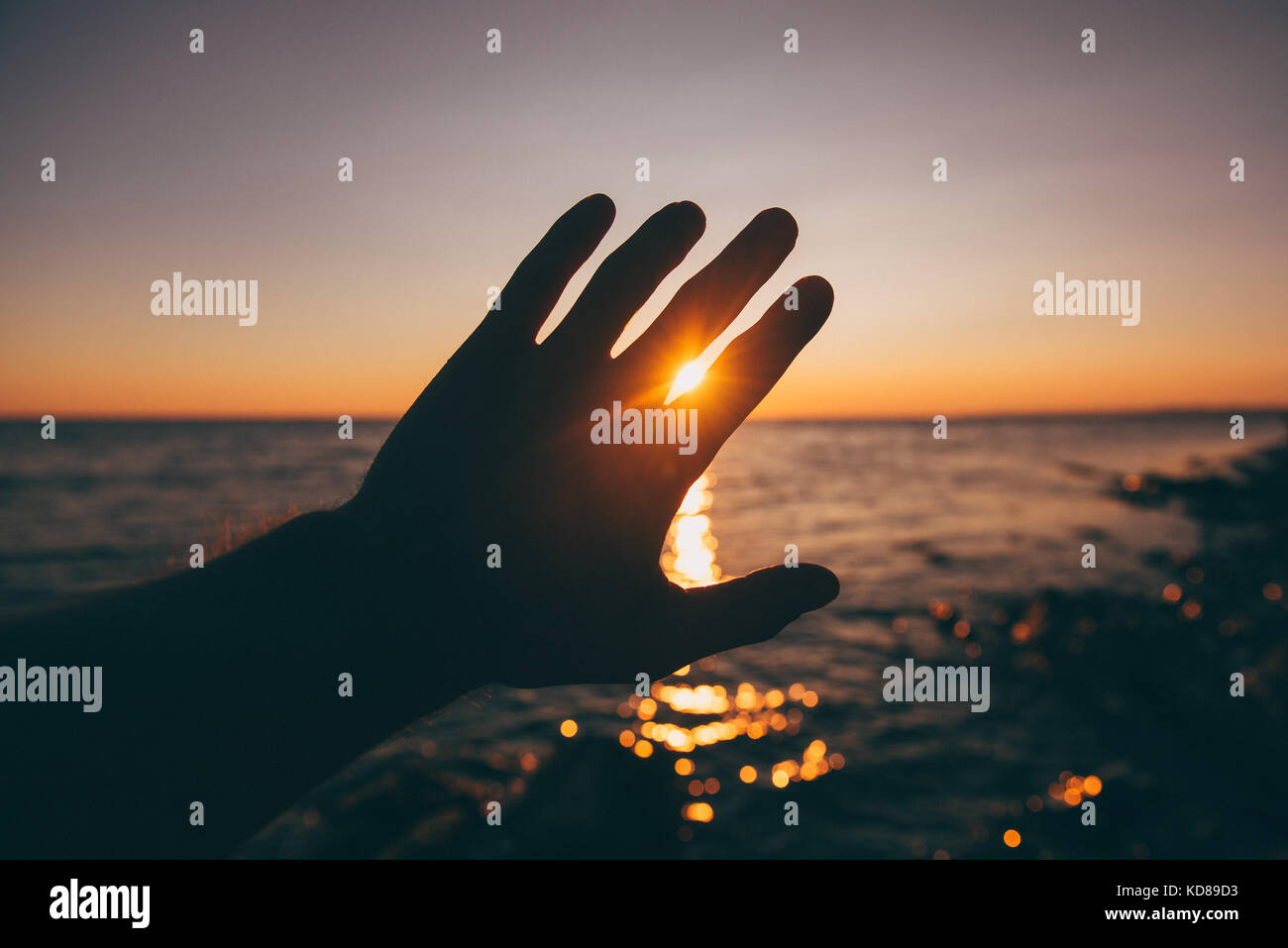 Silhouette of a hand in front of the sun at sunset Stock Photo