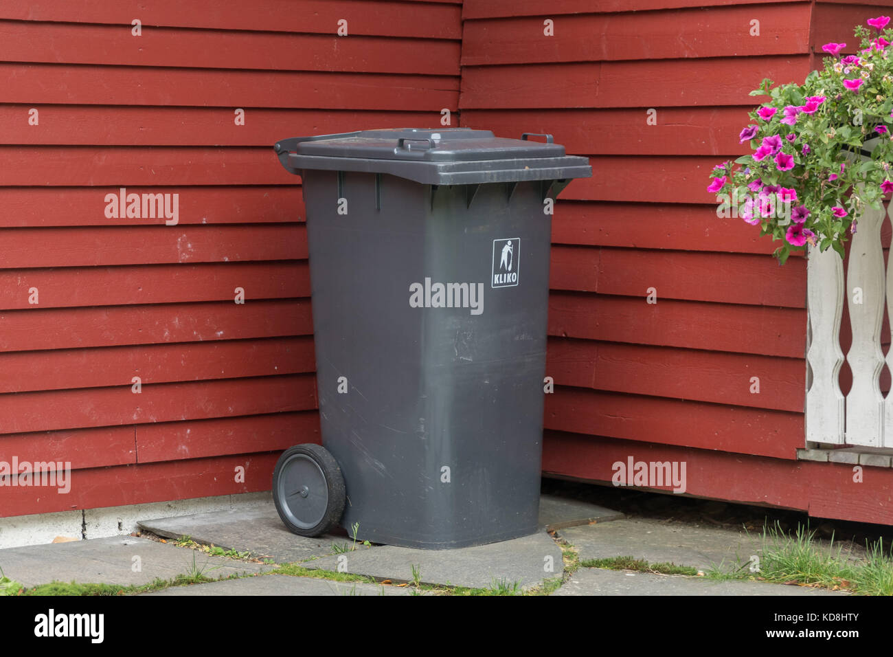 Plastic garbage bin trashcan outside a red walled house Stock Photo