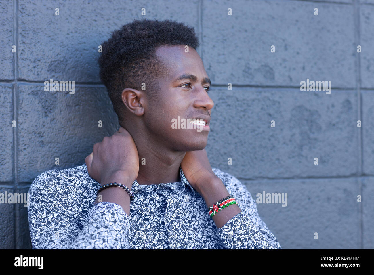 Handsome young black man stands in front of gray block wall with hands on neck Stock Photo