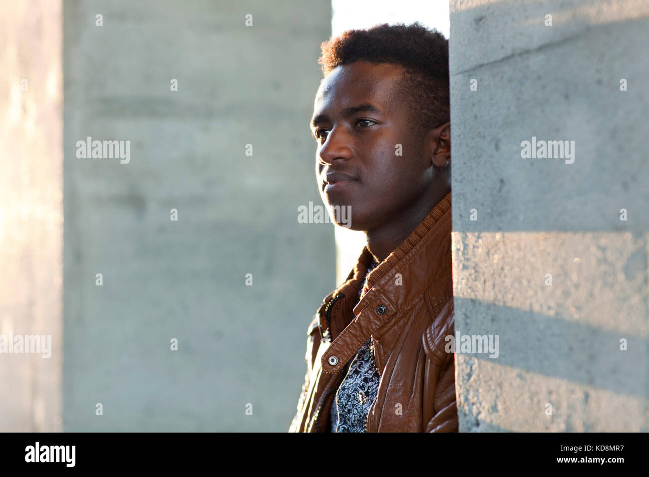 Handsome young black man stands in sunlight between concrete pillars Stock Photo